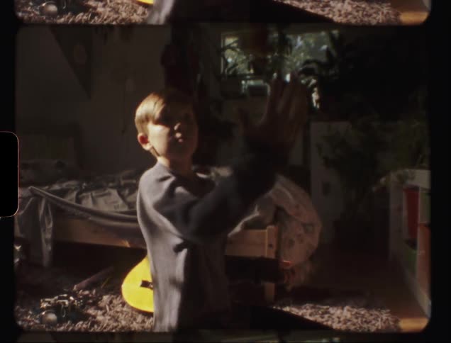 Young boy juggles a ball while sitting on a bedroom floor