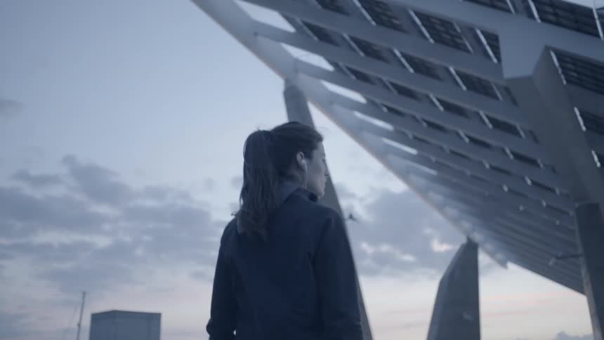 Woman walks outside near leaning structures at sunset