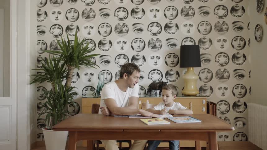 A man sits at a table helping his son with school work
