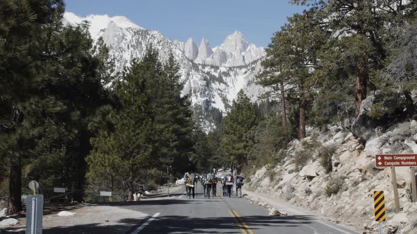 Group of people walk down a street surrounded by trees and mountains