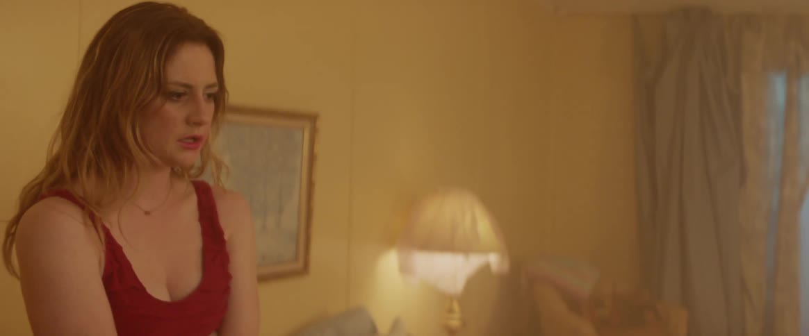 Woman stands in a room looking upset and wipes her face
