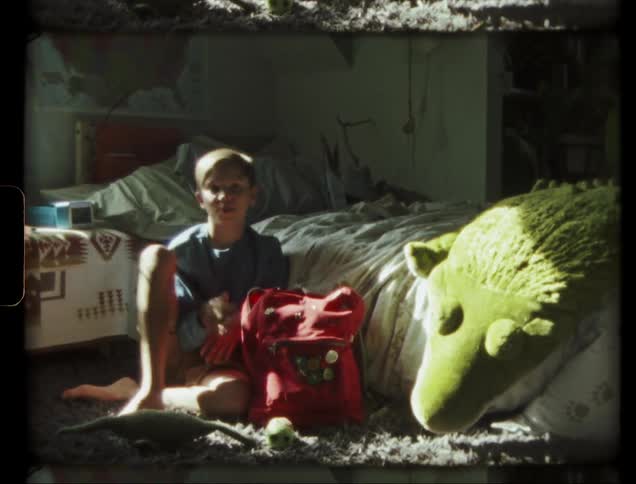 A boy is removing items from his backpack as he sits in his room in daylight