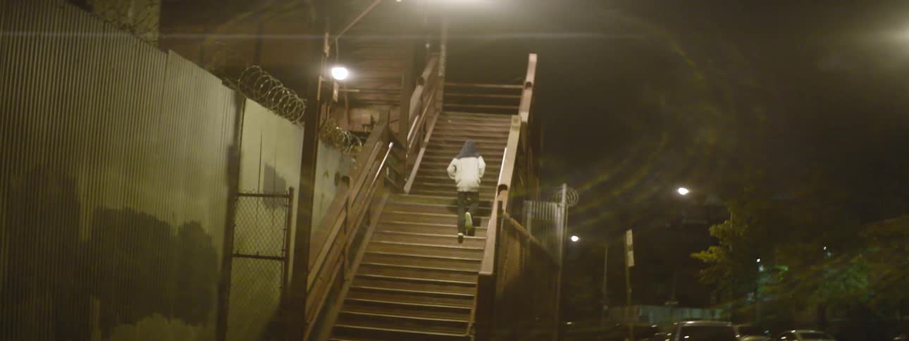 Someone wearing a hoodie trots up stairs in a deserted area of the city at night