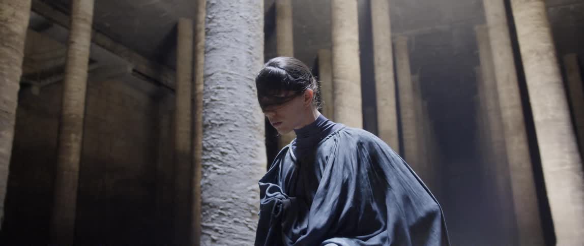 Person wearing a black cape dances near pillars