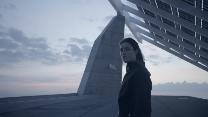 Woman stands outside near crooked structures at sunset