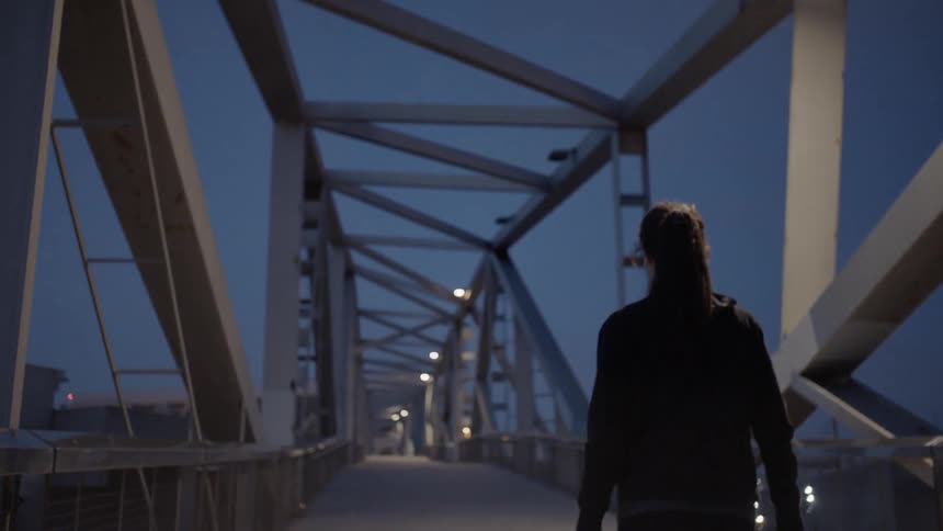 Woman walking across a foot bridge at dusk