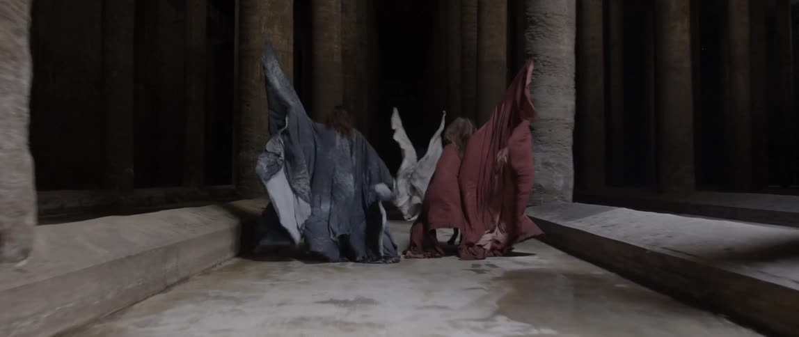 Three women in robes running through ruins
