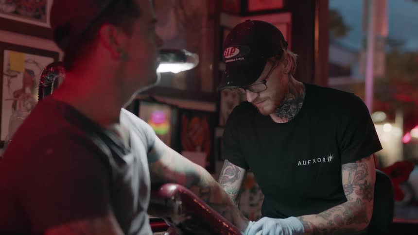 Man gets a tattoo done by another man in a shop
