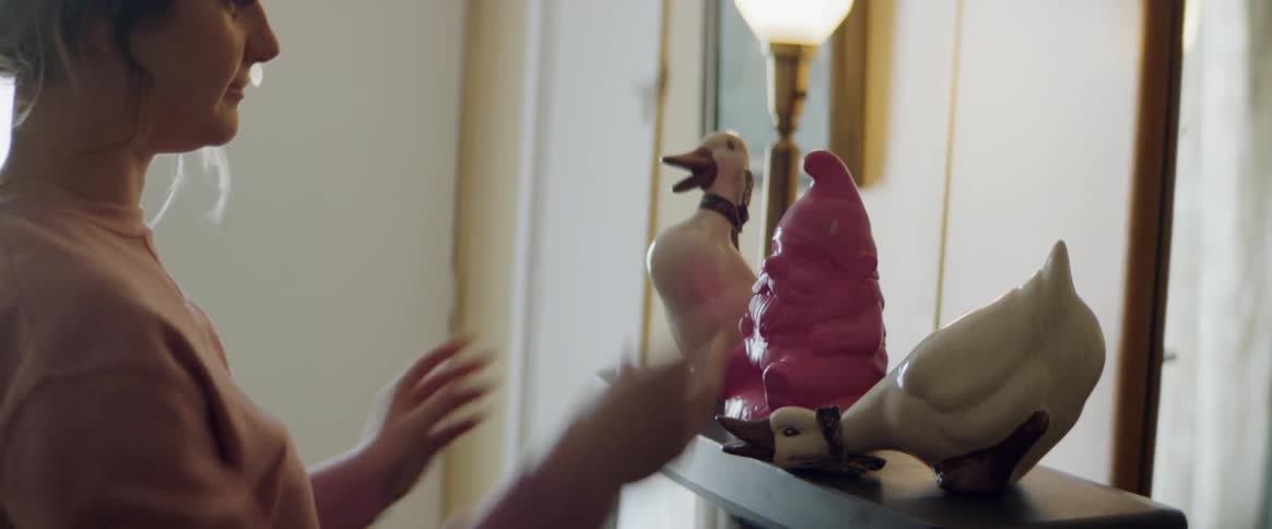 A woman is arranging ceramic statues on top of a television in daylight