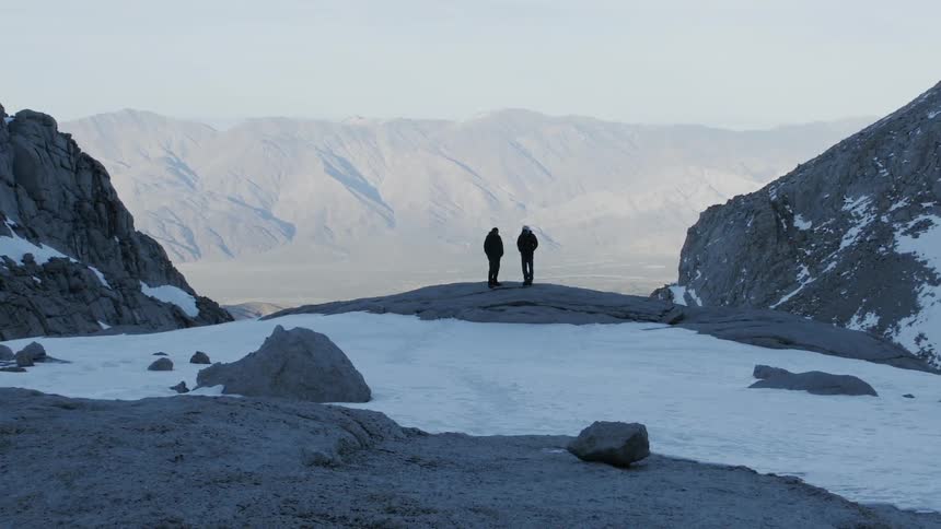 Two men stand atop a mountain