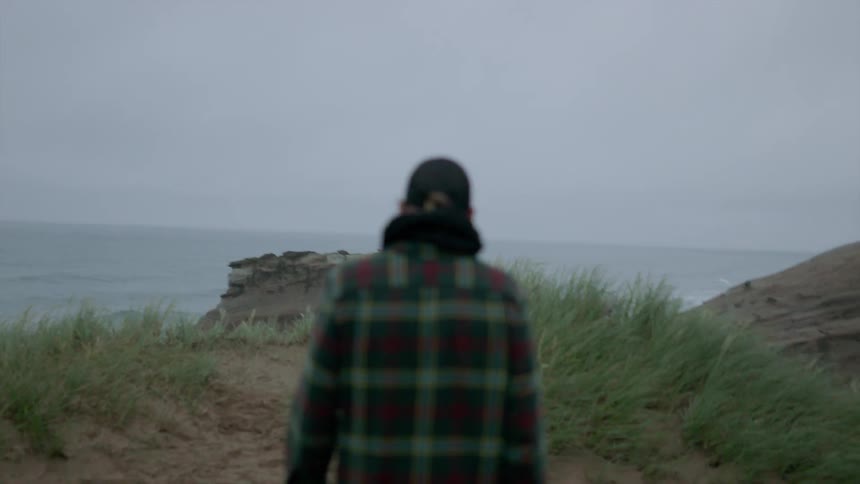 Woman walks towards a cliff's edge overlooking a large body of water