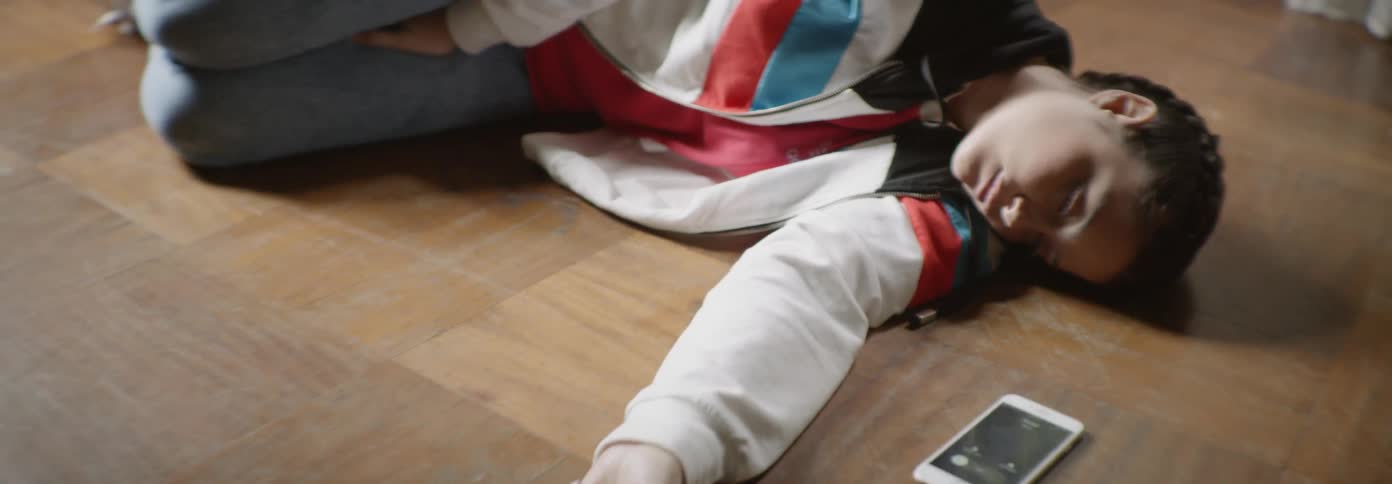 A woman lies on a wood floor next to a smartphone