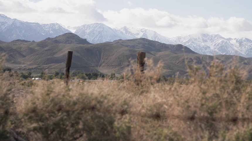 Crooked fence runs through tall grasses with mountains in the background