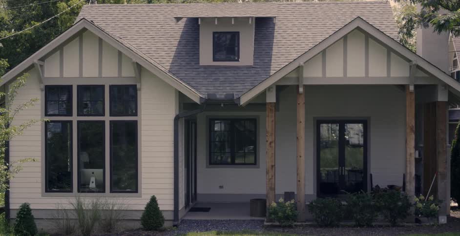 A computer monitor and movement are visible through a house's front window