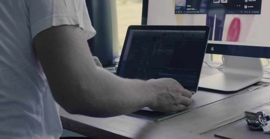 A man is plugging in his laptop as he sits at a desk in daylight