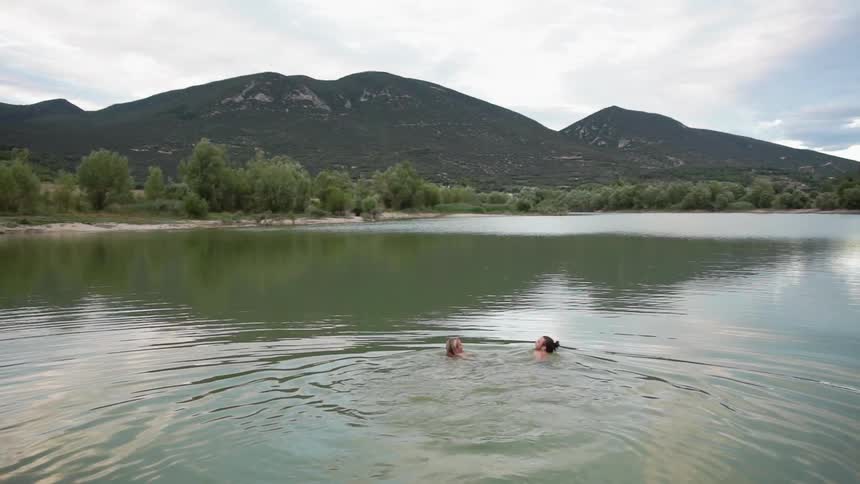Man and woman are swimming in lake on cloudy day