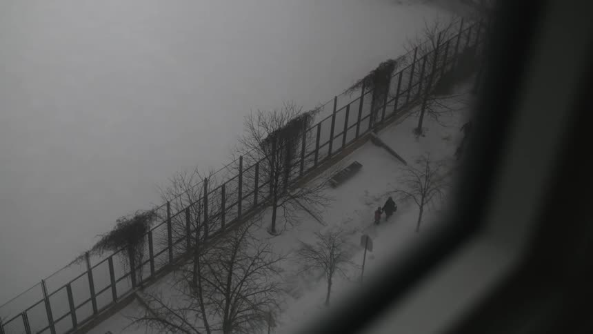 Looking out a building window onto people walking down a snow-covered sidewalk