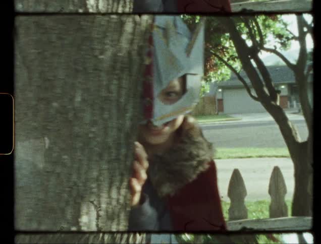 Child wearing a mask hides behind a tree and looks out