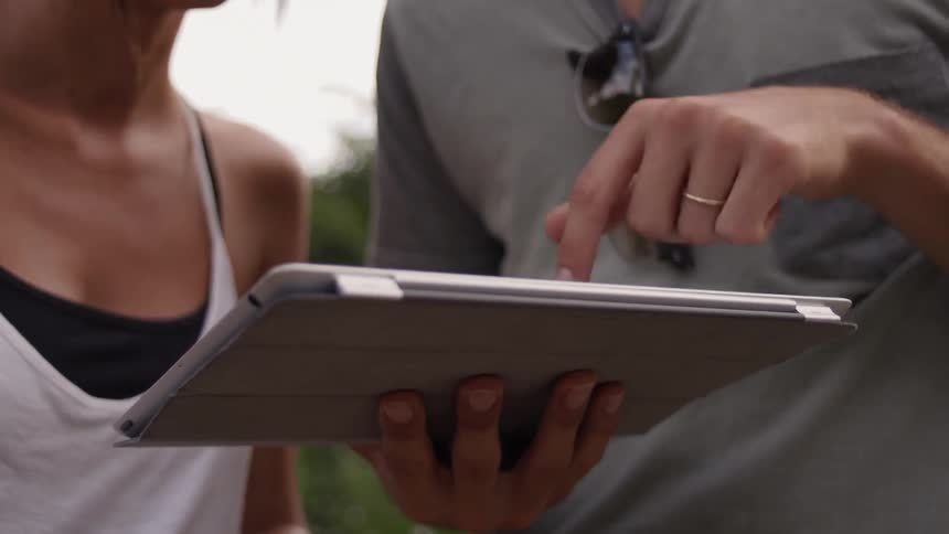 A man and woman use a tablet outside