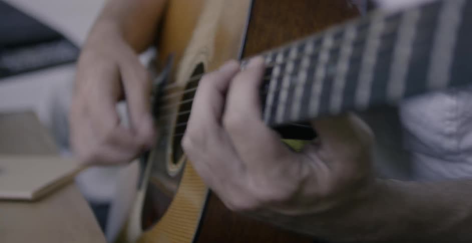 Man strums a guitar sitting near a table