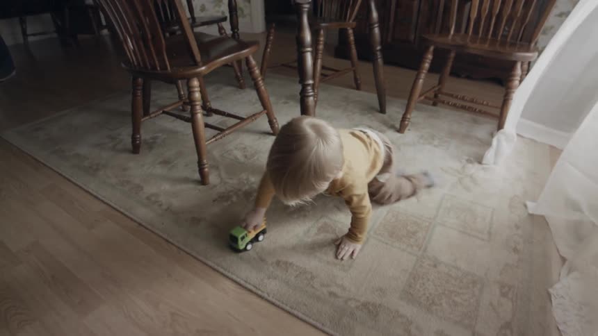 Toddler boy plays with a toy car in a dining room