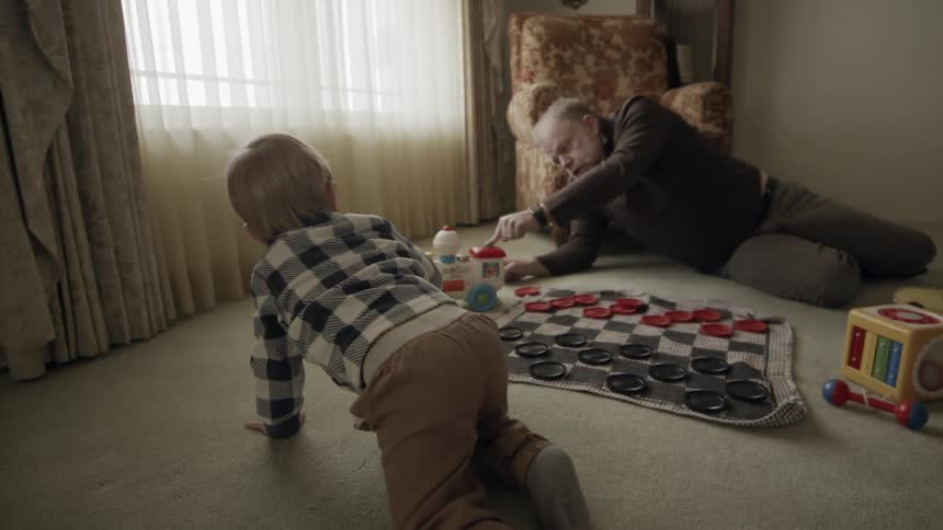 Man and toddler boy play on a living room floor