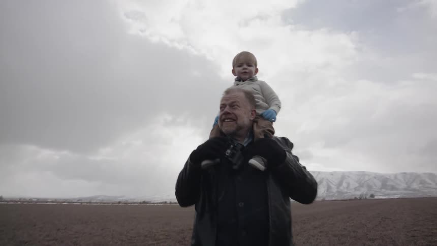 Man stands in a field with a child on his shoulders