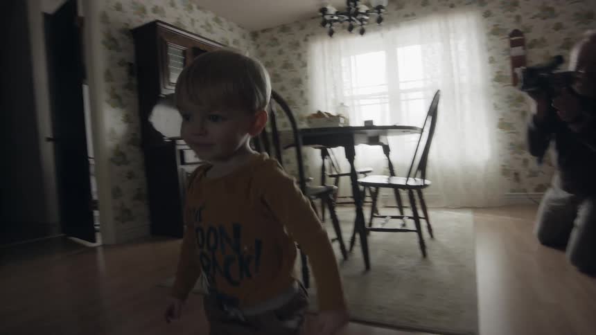 An elderly man films a young child walking in the house