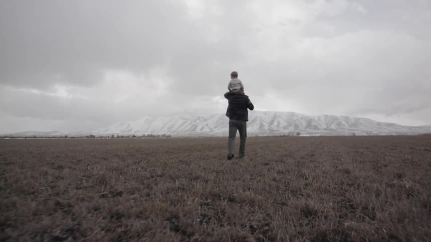 Man walks in a rural field with a baby on his shoulders