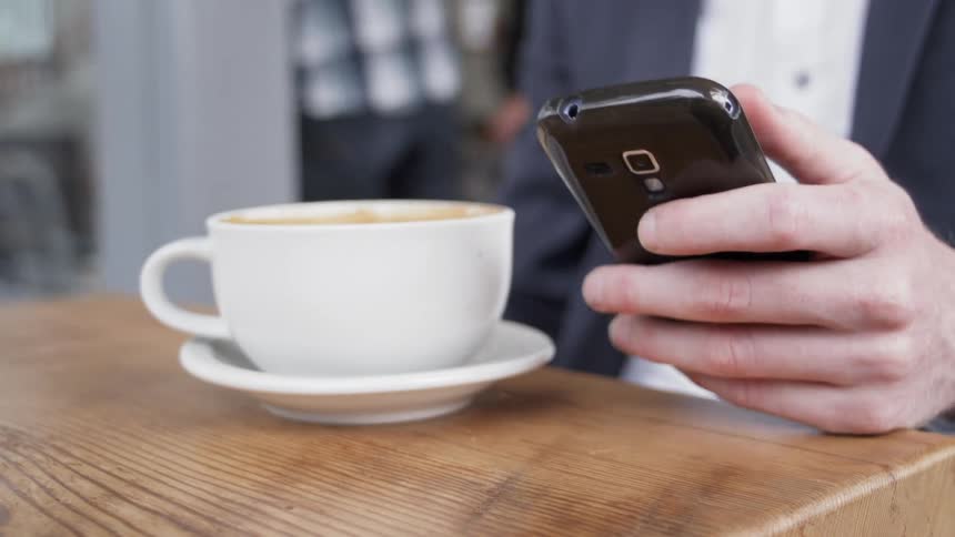 Person sitting at a table with a cup of coffee picks their phone up