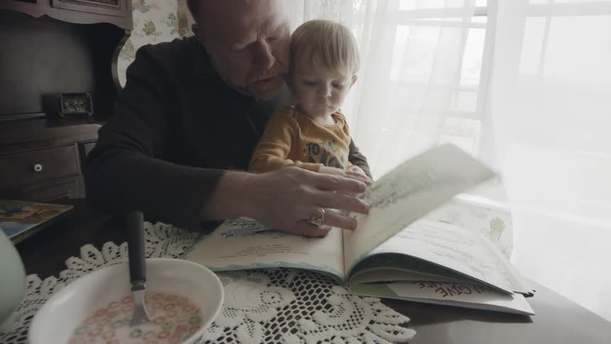 Man and toddler boy read a book at breakfast