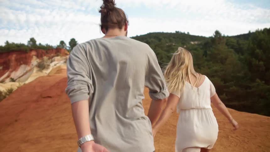 Woman and man hold hands and run on a sandy hill