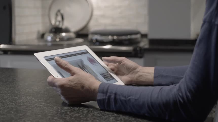 A woman is scrolling through a screen on a tablet inside her kitchen at night