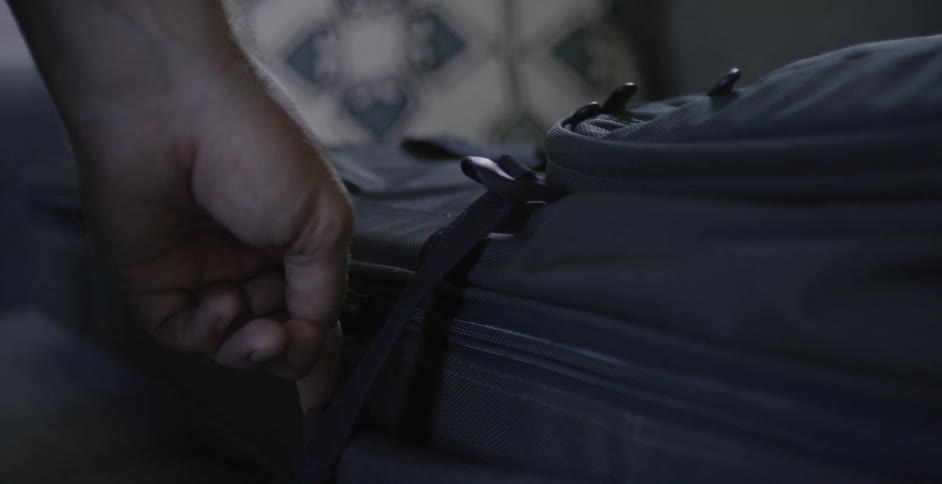 A person is unzipping a suitcase inside in daylight