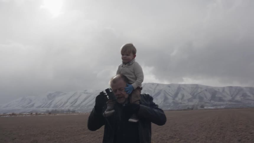 A grandpa is carrying his grandson on his shoulders in a natural environment on a cold day