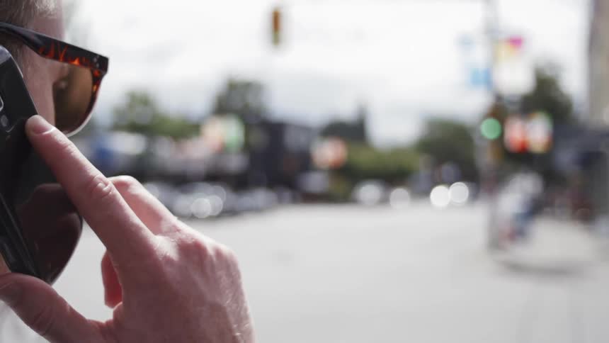A man is walking through an intersection holding his cell phone to his ear in daylight