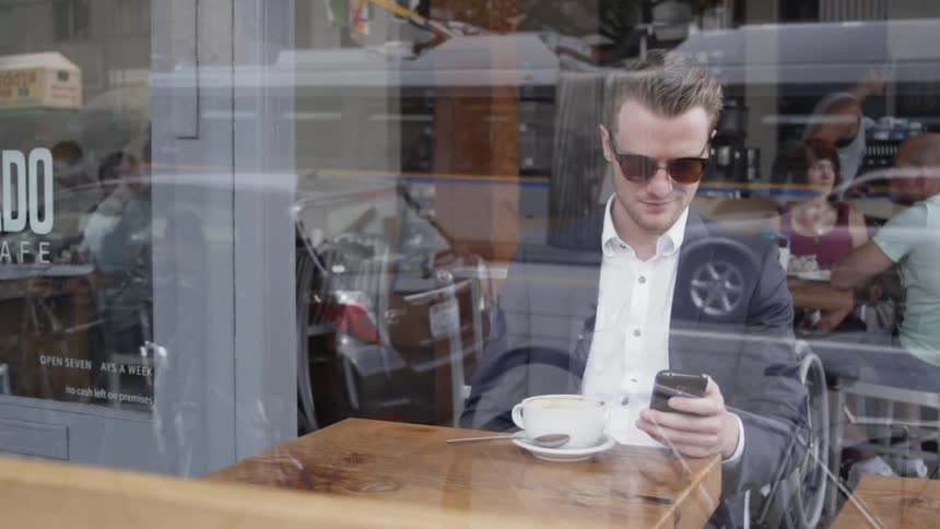 Man holds his phone while drinking coffee in a coffee shop