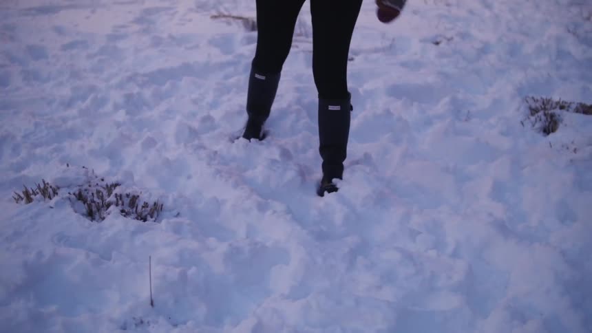 A woman wearing knee-high boots walking through the snow and kicking it up