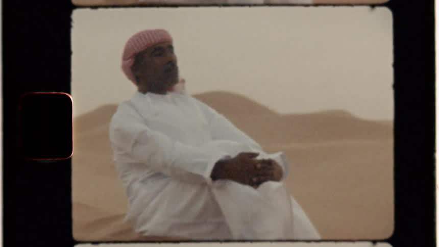 Sand is blowing around a middle eastern man as he sits outside in daylight