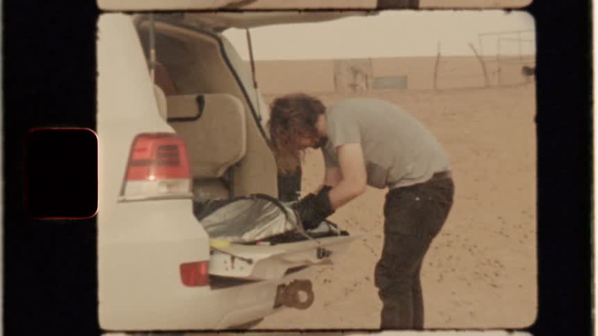 A man works on something inside a plastic bag in the back of an suv