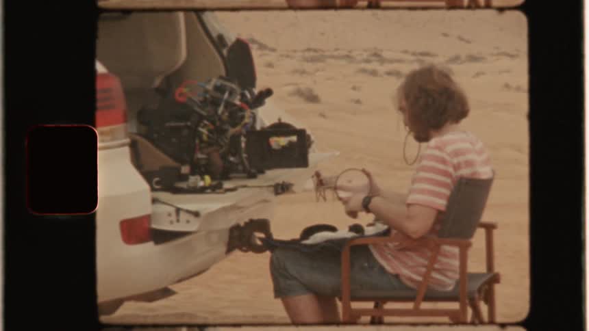 A man sits in a chair adjusting filming equipment