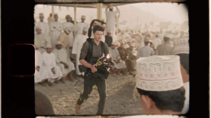 Man holding video camera walks through crowd of muslim men