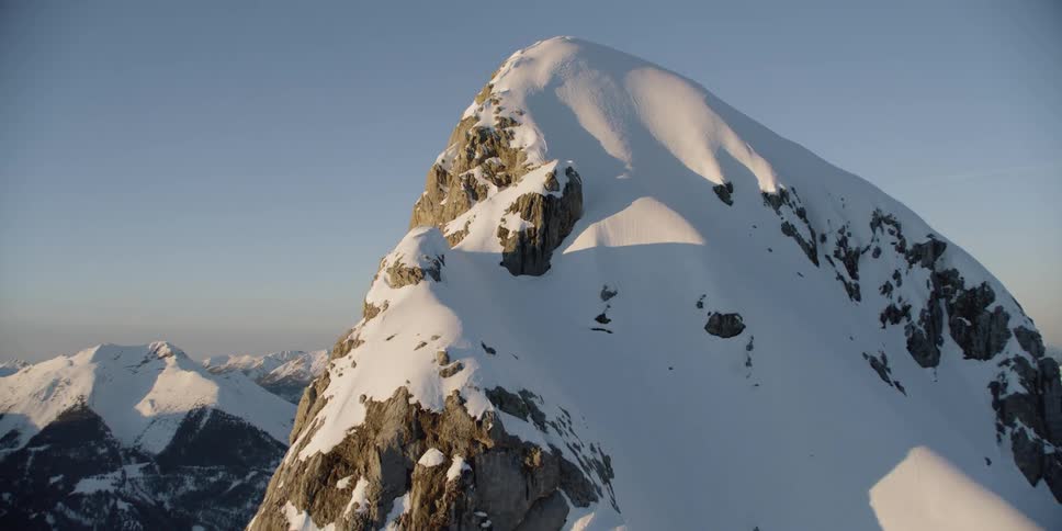 A cross is standing on a high mountain peak in a mountain range during the day