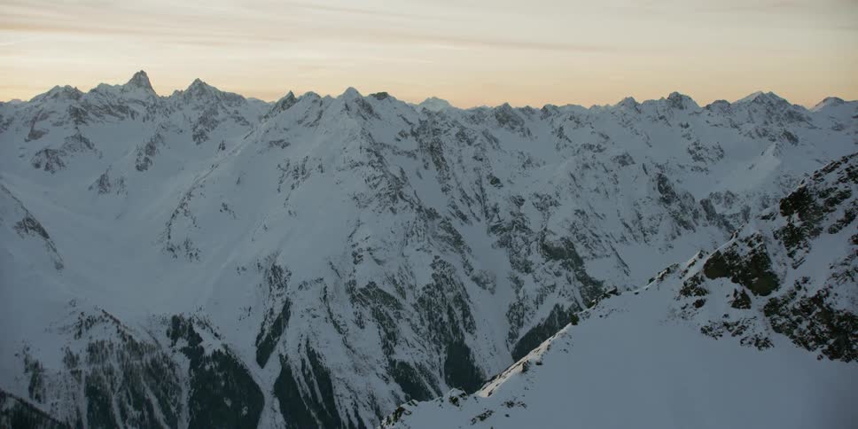 Dawn is breaking over a snow-covered mountain range
