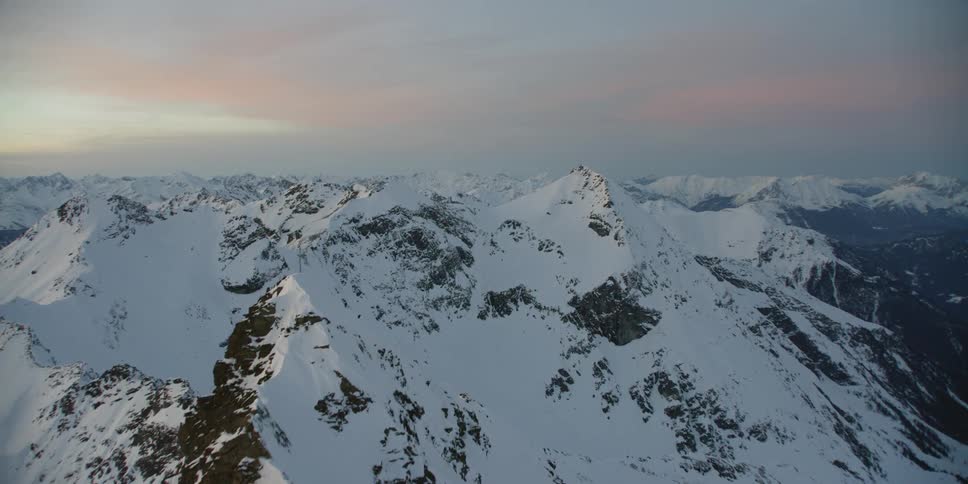 Sun sets over snowy mountains on a cloudy evening