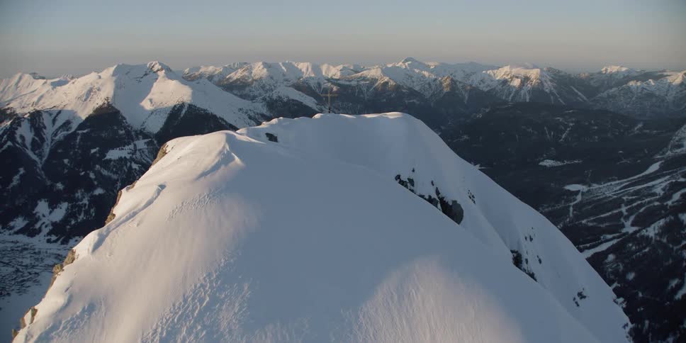 A cross sits on a snowy mountain peak
