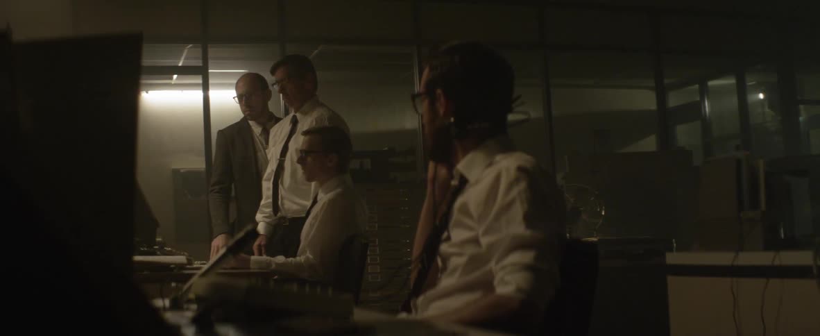 For men in a dark office study something on a screen