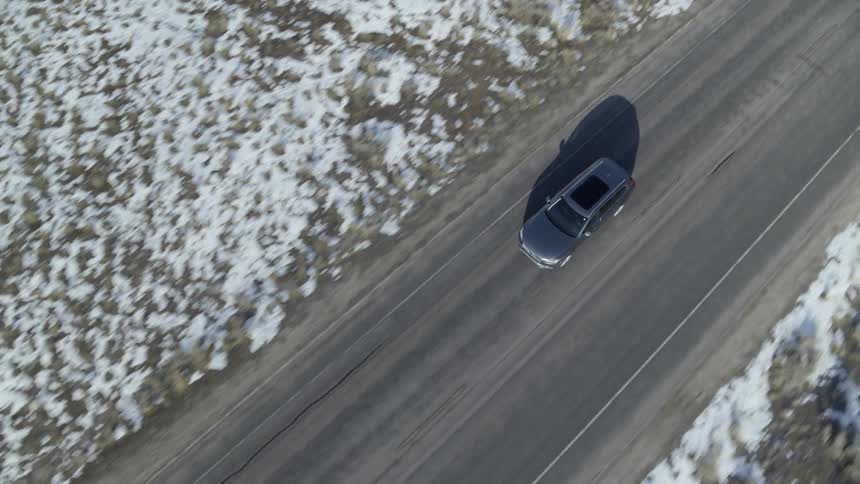 Vehicle travels down the road near a snow covered field