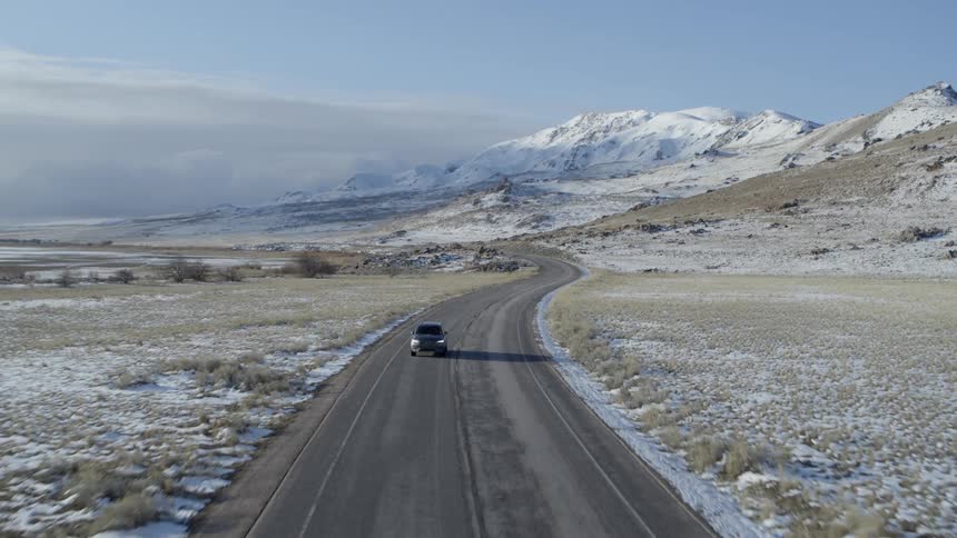 Car drives on a rural road near snowy mountains