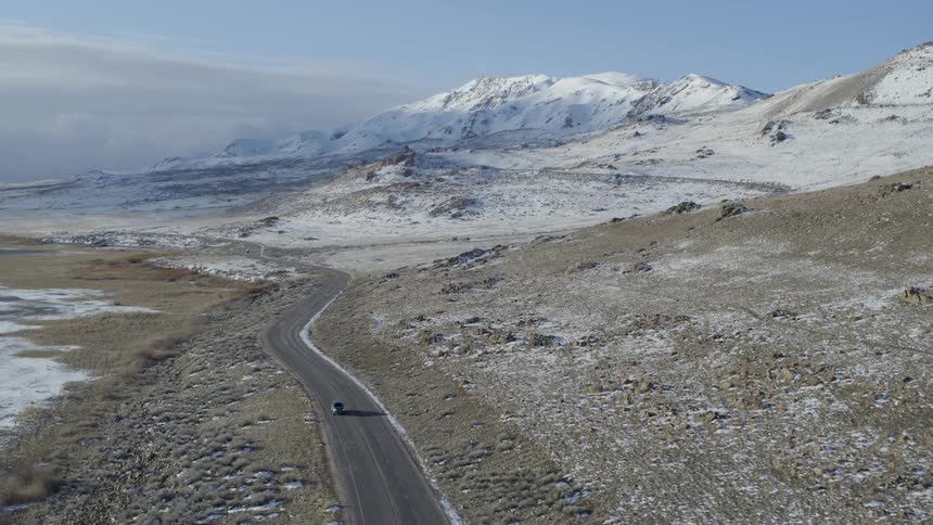 A car travels on a rural road near snowy mountains